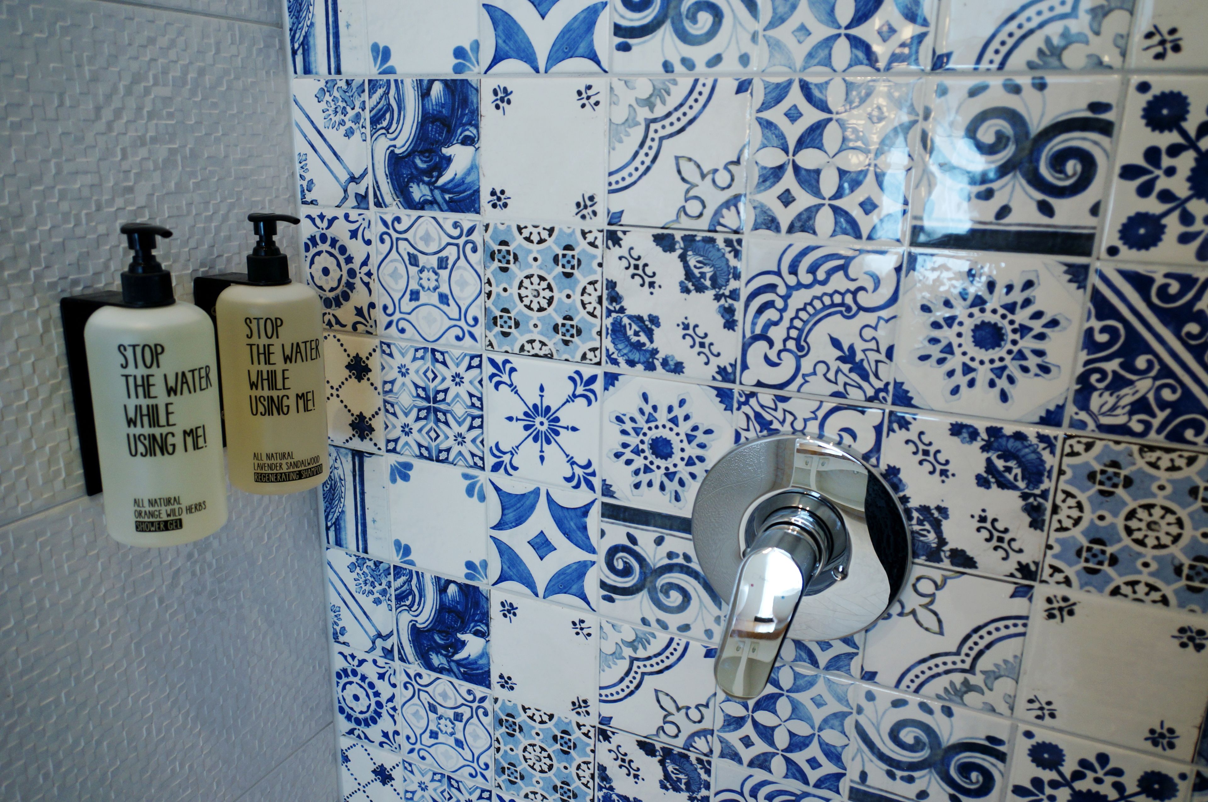 Une salle de bain avec des carreaux bleus et blancs formant un motif, un distributeur de savon fixé au mur et un robinet.