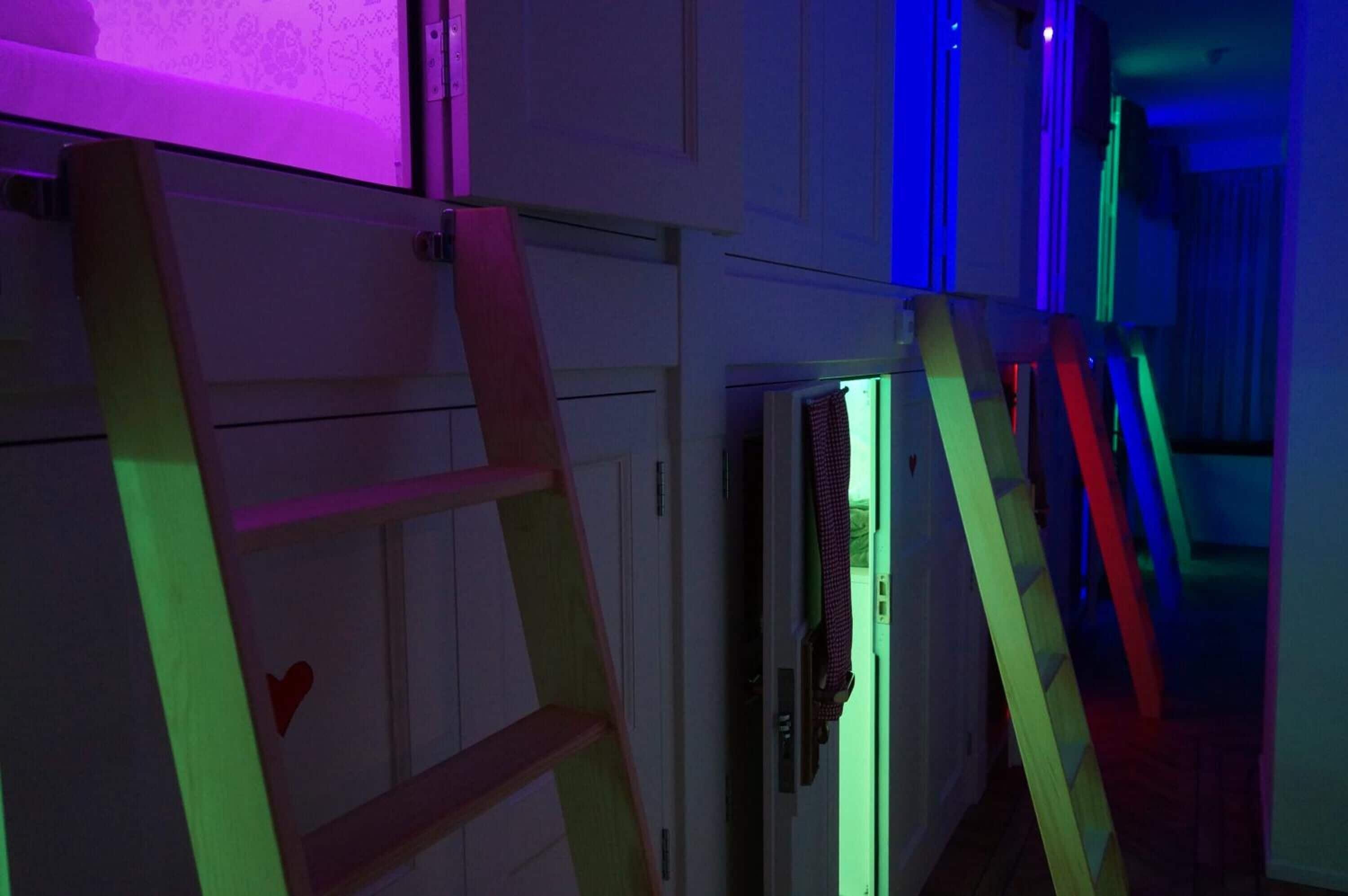 Ein Zimmer mit einer an der Wand angelehnten Holzleiter, einem Fenster mit violetter Beleuchtung und einer Tür mit grünem Licht.
