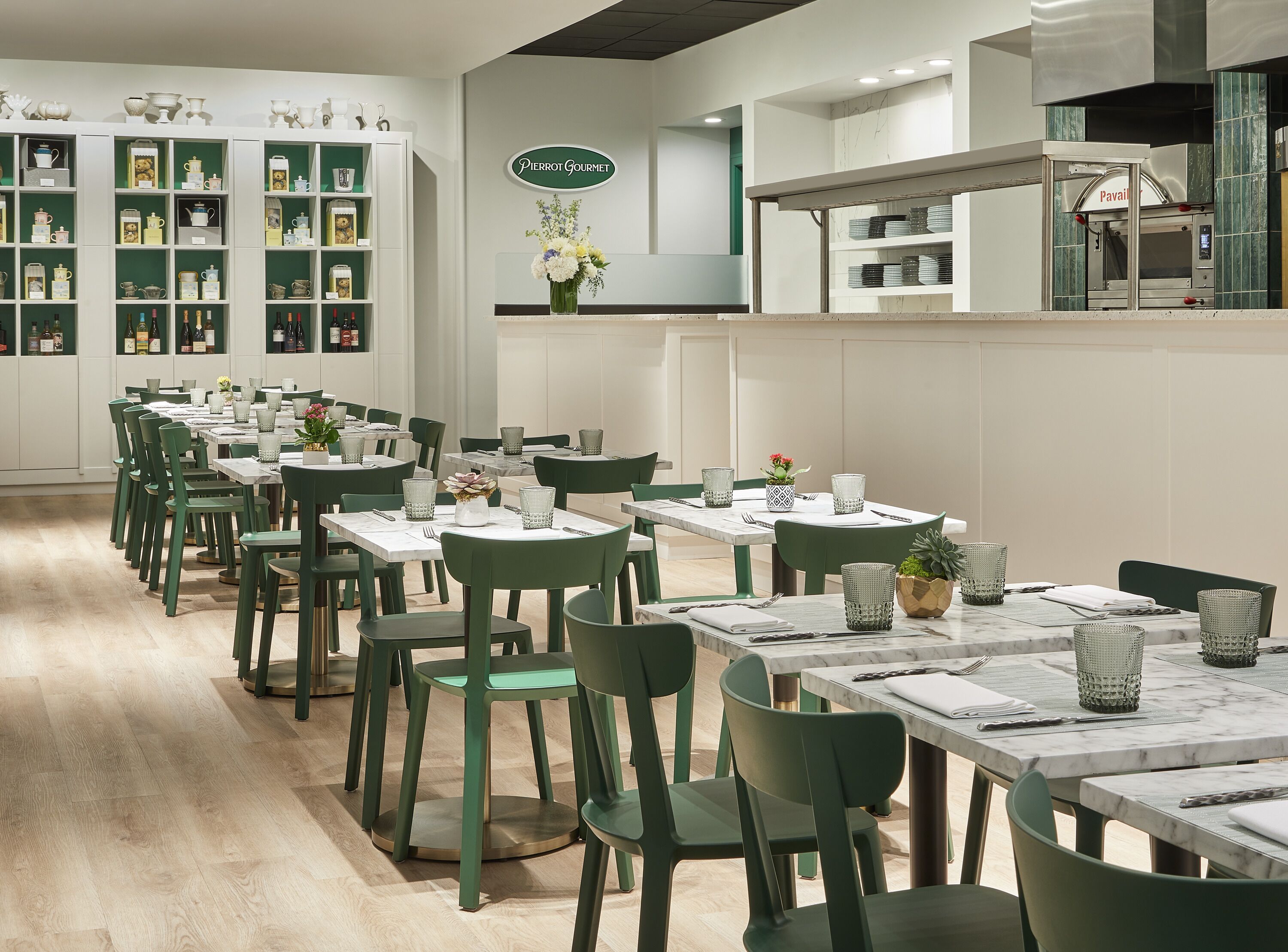 A restaurant with green chairs and tables, a display of kitchenware, and a sign for Pierrot Gourmet.