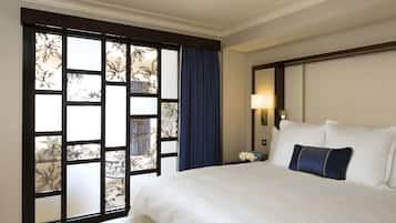 A hotel room with a large bed, a nightstand, a lamp, and a view through a window with a floral pattern.
