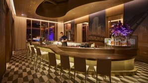 Eine moderne Bar mit Schachbrettmuster-Boden, Barhocker und einem Barkeeper.