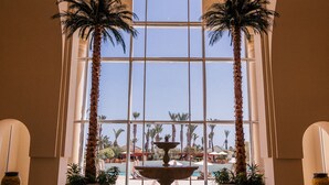 A lobby with a large arched window, palm trees, a fountain, and a reflection on the polished floor. - The Residence Tunis (La Marsa)