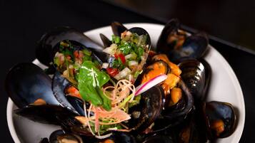 Un plato de mejillones acompañados de vegetales y hierbas, junto a una porción de papas fritas y tomates cherry sobre un fondo oscuro.