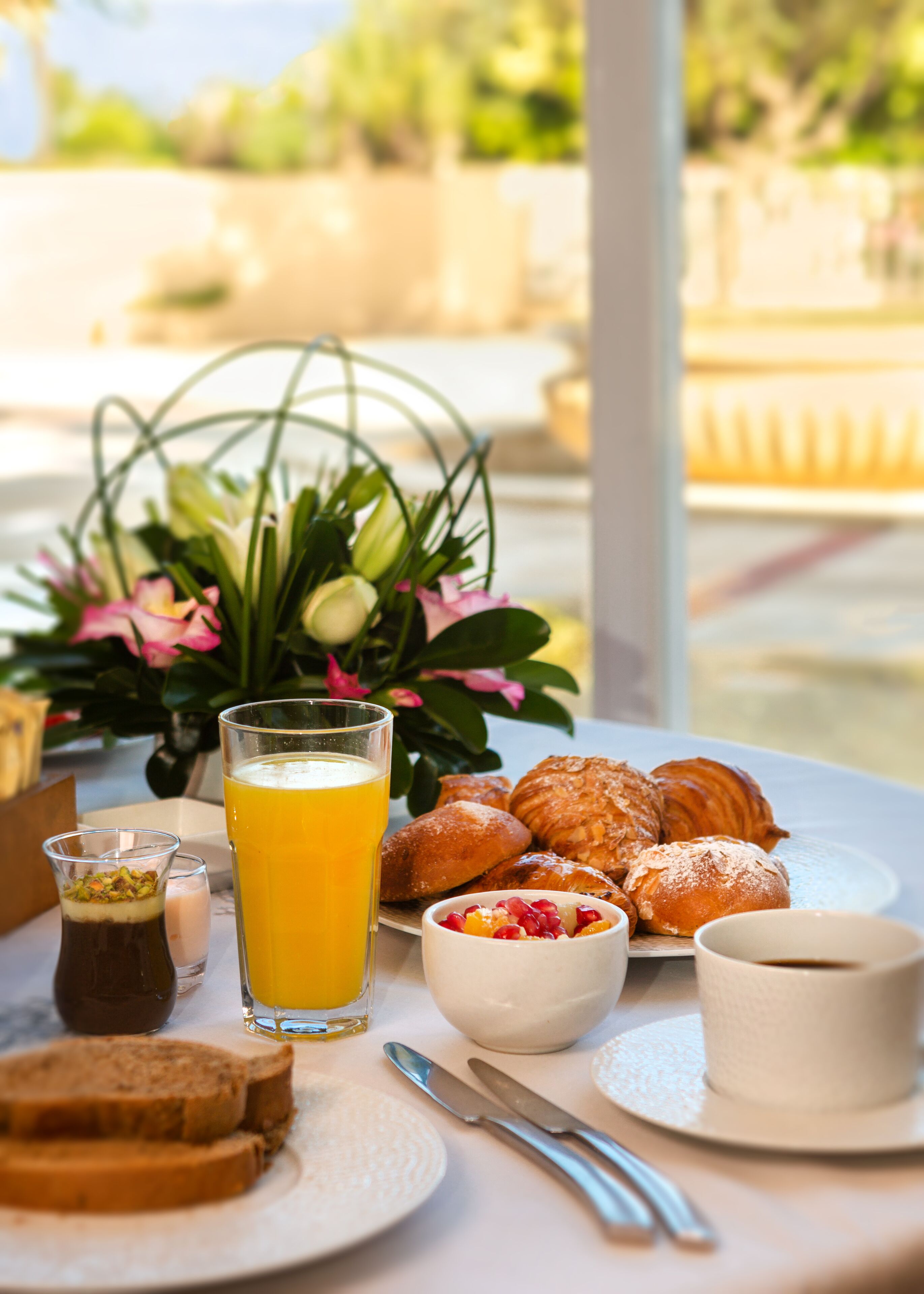 Une table de petit-déjeuner avec des croissants, un verre de jus d’orange, un petit bol de fruits et une tasse de café.