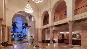 A spacious lobby with high ceilings, large chandeliers, and palm trees. - The Residence Tunis (La Marsa)