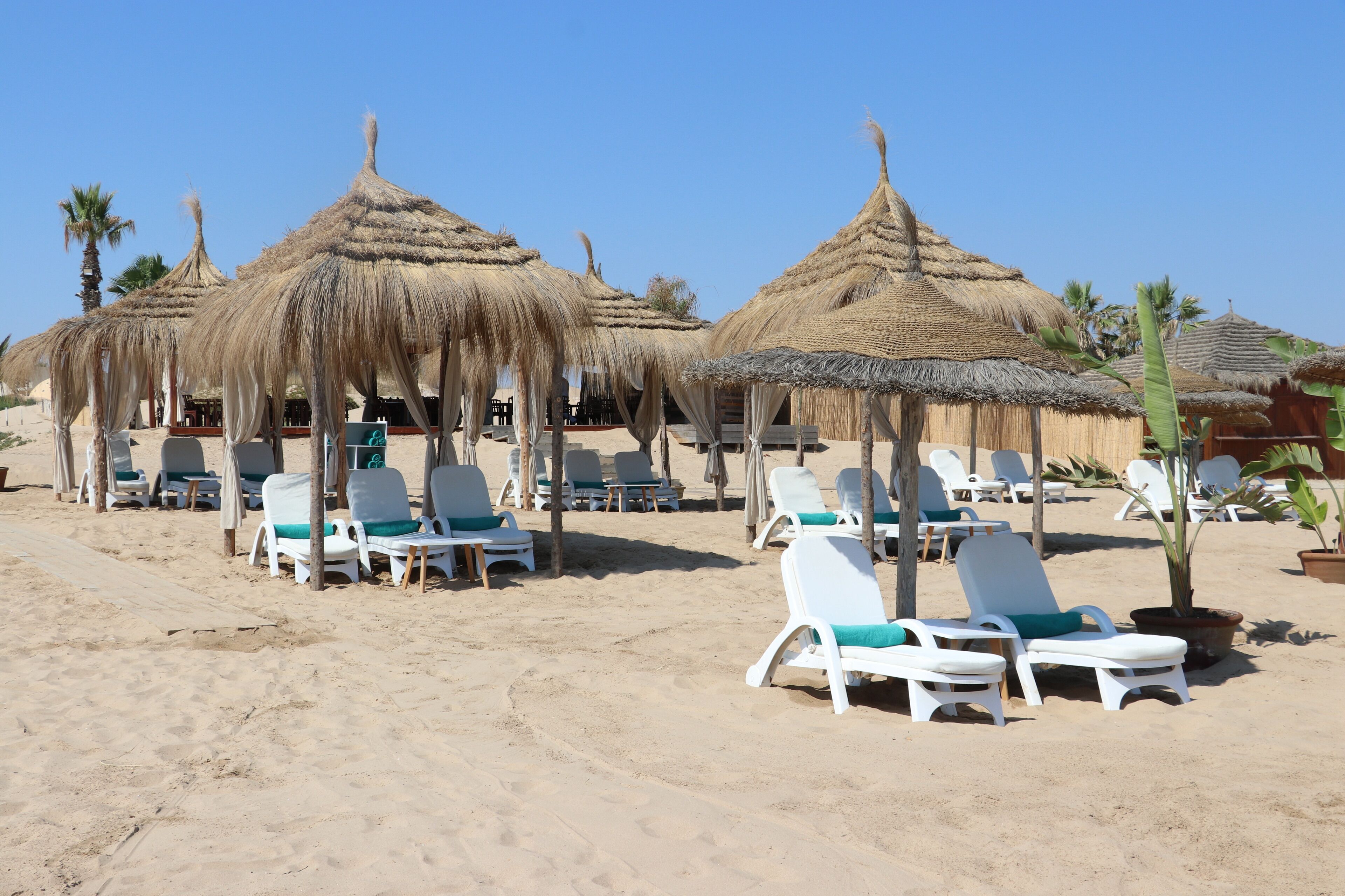A beach with thatched umbrellas and white lounge chairs.