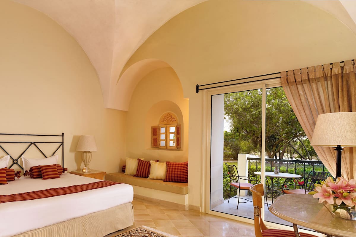 A bedroom with a bed, bedside tables, a window, and a balcony with a table and chairs.