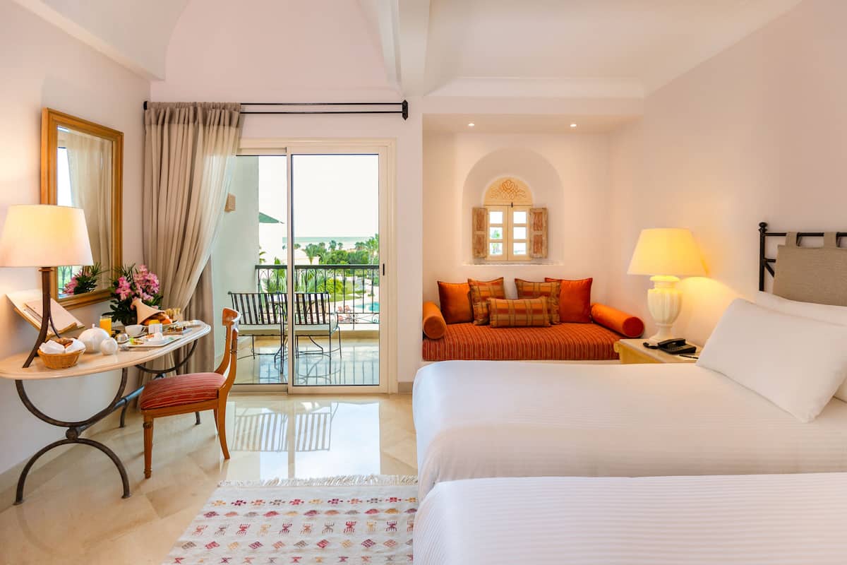 A hotel room with a balcony, a dining area, and a bed with pillows.
