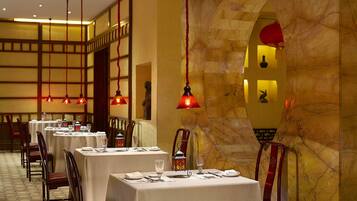 Un restaurante con varias mesas, lámparas rojas colgantes y una pared de mármol.