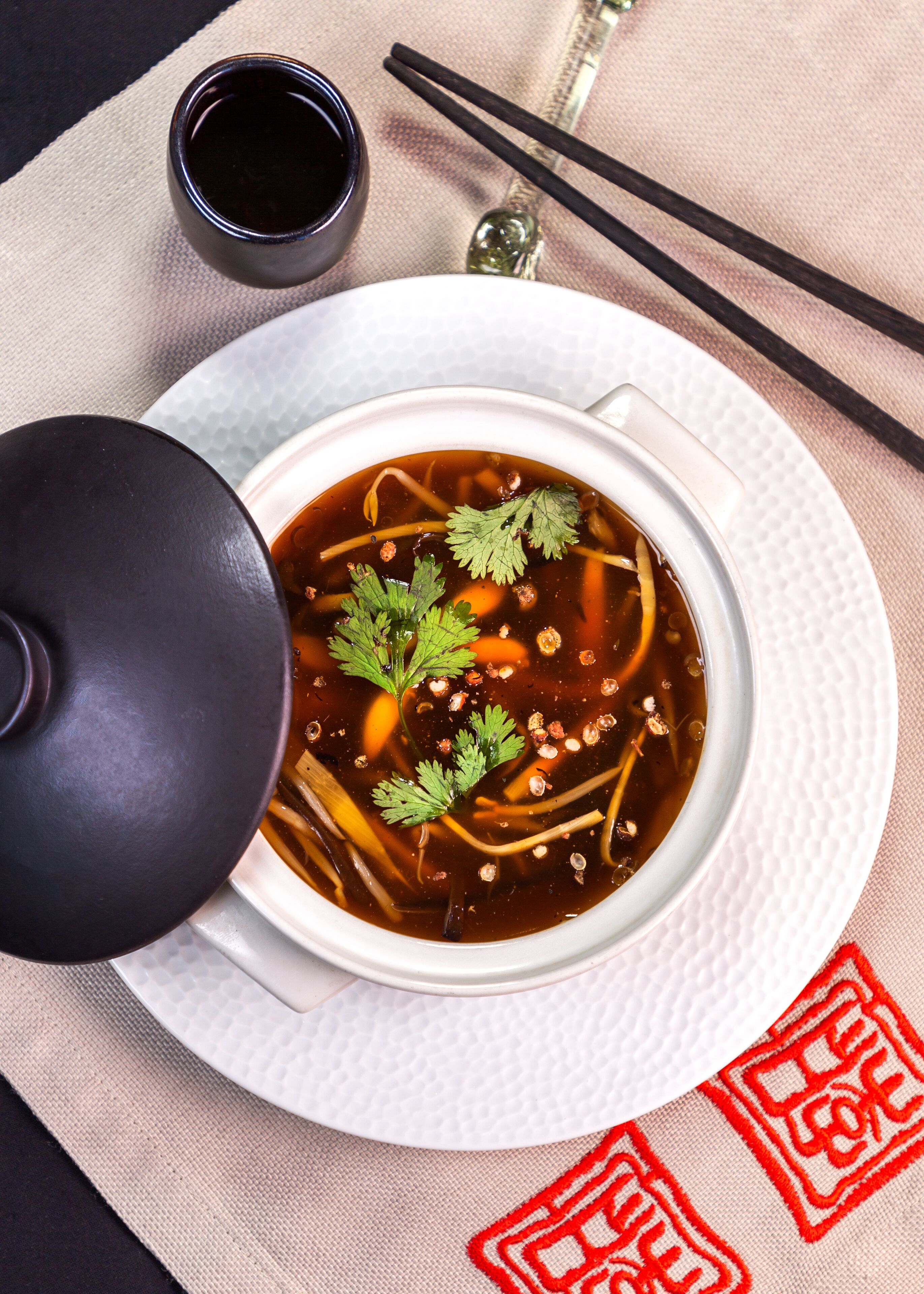 Un bol de soupe, des baguettes et une petite tasse à côté.