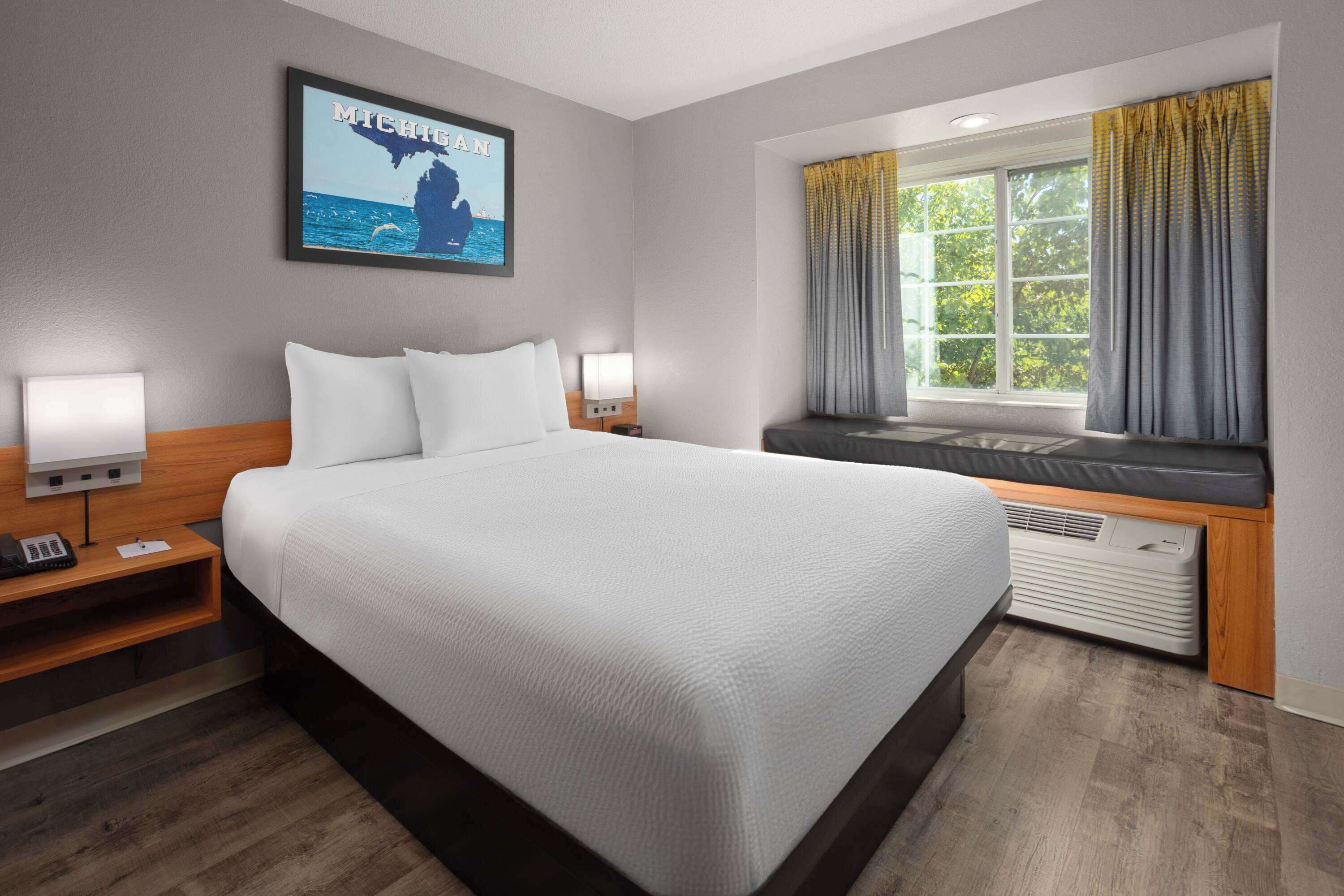 Habitación de hotel con una cama grande, dos mesitas de noche con lámparas, una ventana con cortinas y un cuadro colgado en la pared.