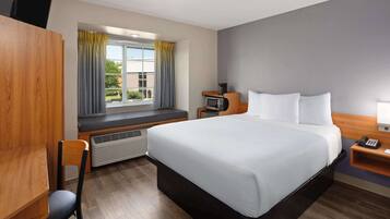 Une chambre d’hôtel comprenant un lit, un bureau, une chaise, un radiateur, une fenêtre avec des rideaux et une petite table avec un téléphone.