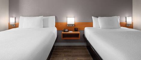 Ein Hotelzimmer mit zwei Betten, einem Holzkopfteil, Nachttischlampen, einem Nachttisch und einer Uhr.