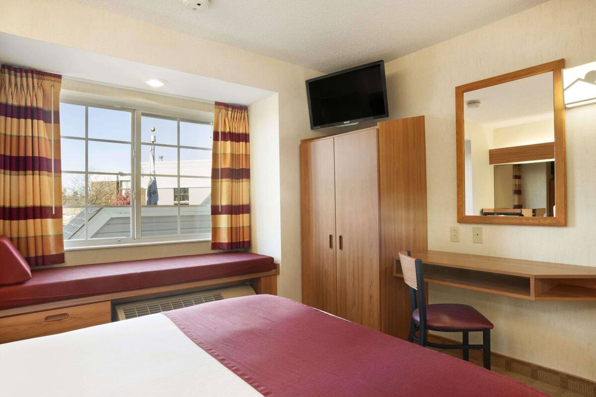 A hotel room with a bed, a desk, a chair, a television, a wardrobe, and a window with curtains.