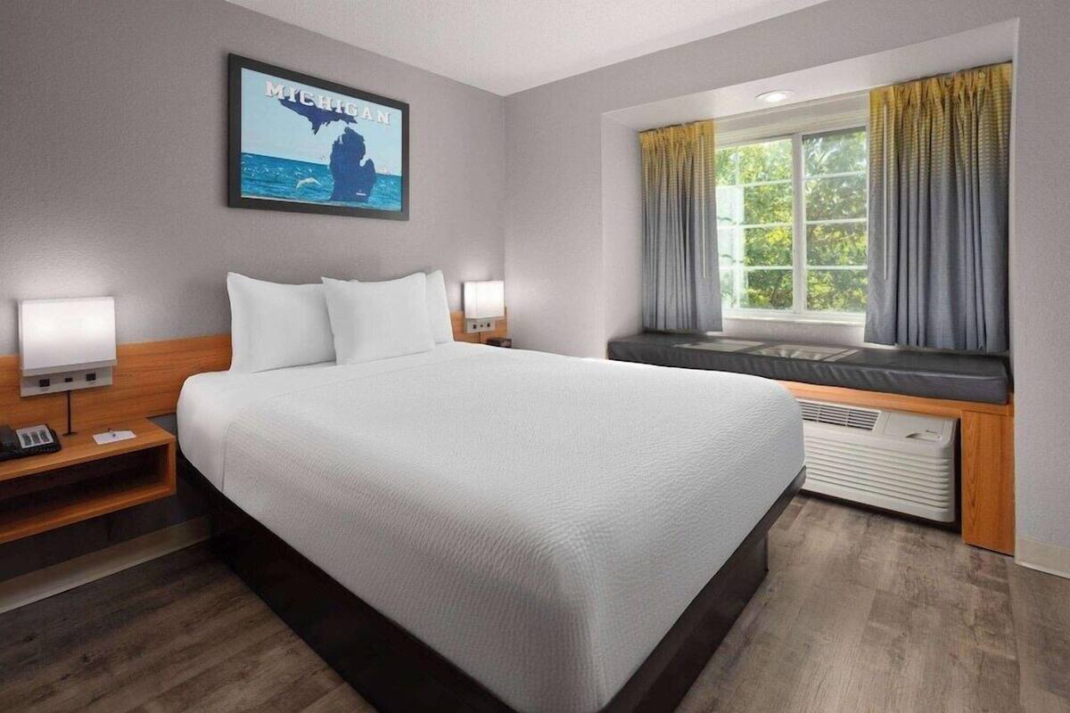 A hotel room with a large bed, bedside lamps, a window with curtains, and a wall-mounted picture.