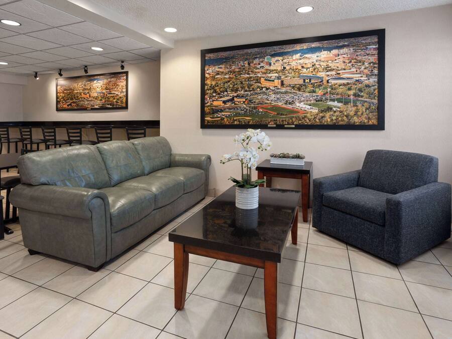 Een hotel lobby met een grijze leren bank, een blauwe fauteuil, een zwarte salontafel en een groot stadsgezicht schilderij aan de muur.