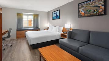 A hotel room with a bed, a sofa, a desk, and a window with curtains.