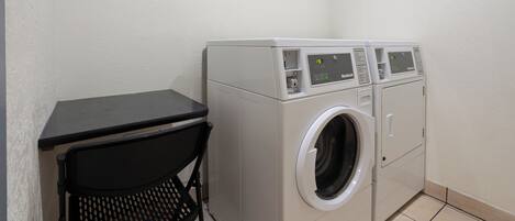 Un espace buanderie compact comprenant un lave-linge, un sèche-linge, une petite table et une chaise.