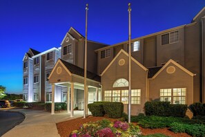 A multi-story hotel with a covered entrance, landscaped gardens, and a clear sky at dusk. - Microtel Inn & Suites by Wyndham Ann Arbor (Ann Arbor)