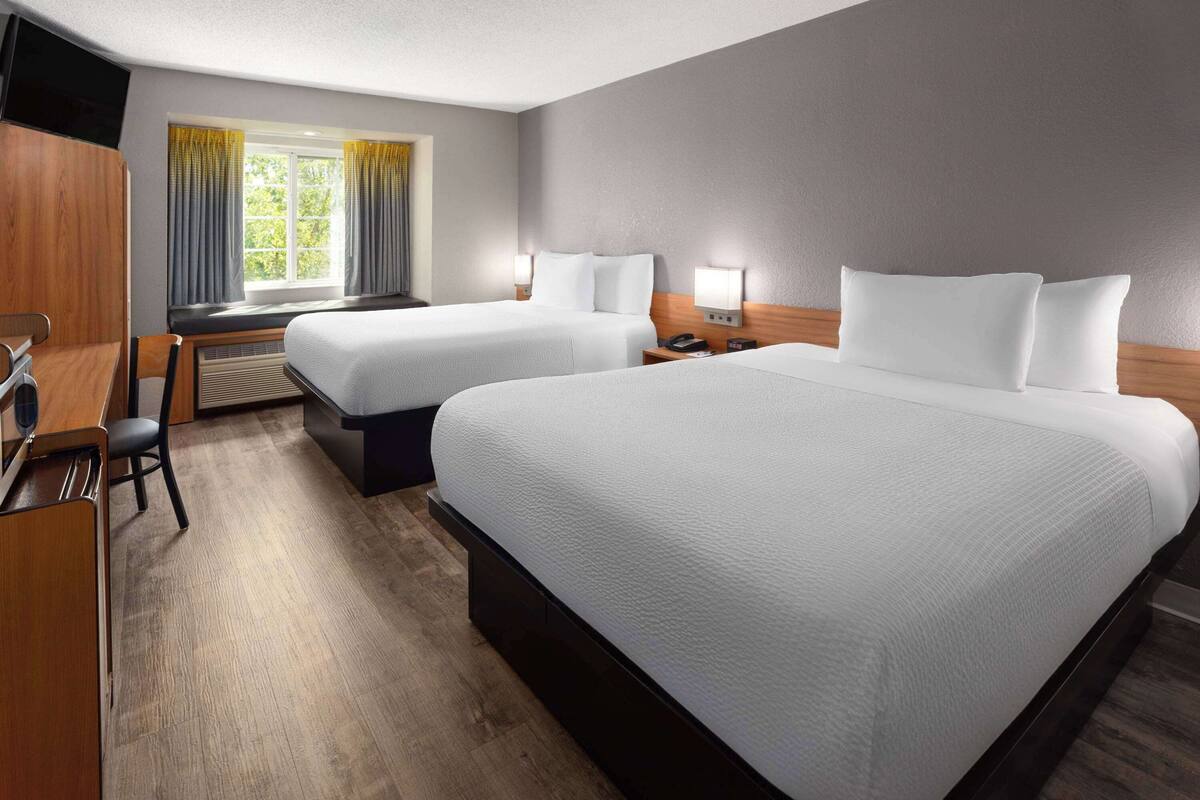 A hotel room with two beds, a desk, a chair, a TV, and a window with curtains.