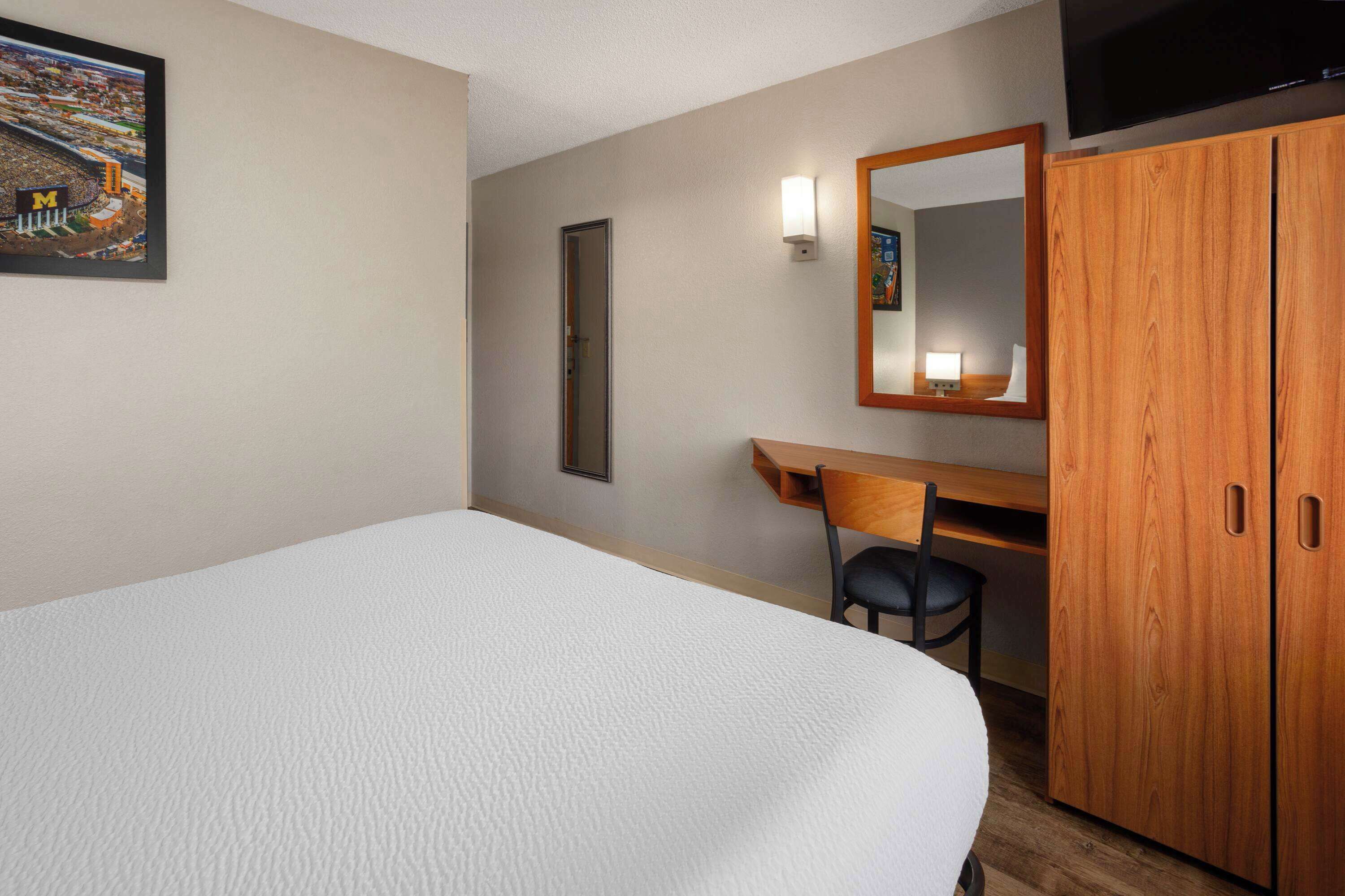 Een hotelkamer met een bed, een bureau, een stoel, een kledingkast, een televisie en een ingelijst schilderij aan de muur.