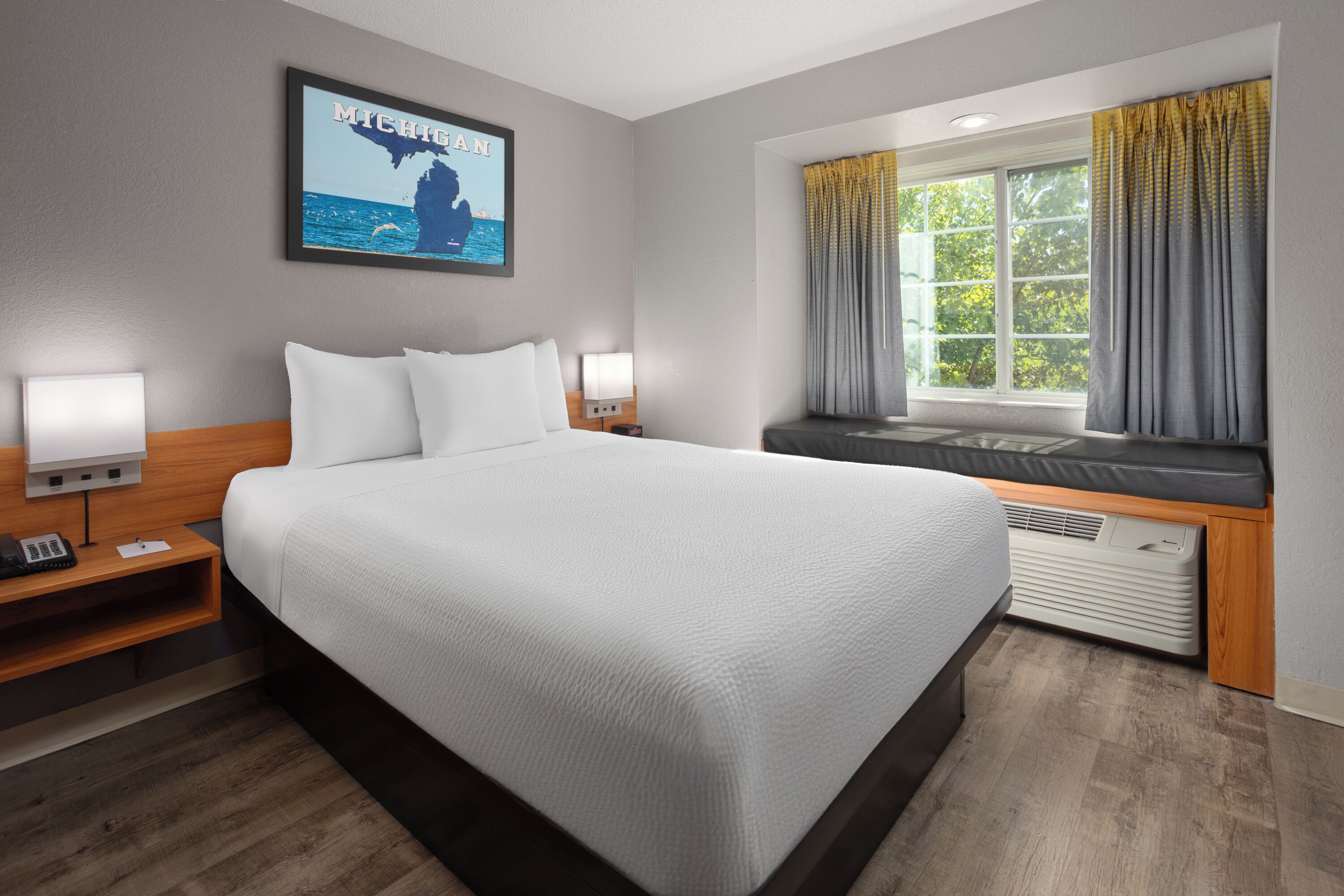 A hotel room with a large bed, a nightstand with a phone, a wall-mounted TV, and a window with curtains.