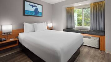 A hotel room with a large bed, a nightstand with a phone, a wall-mounted TV, and a window with curtains.