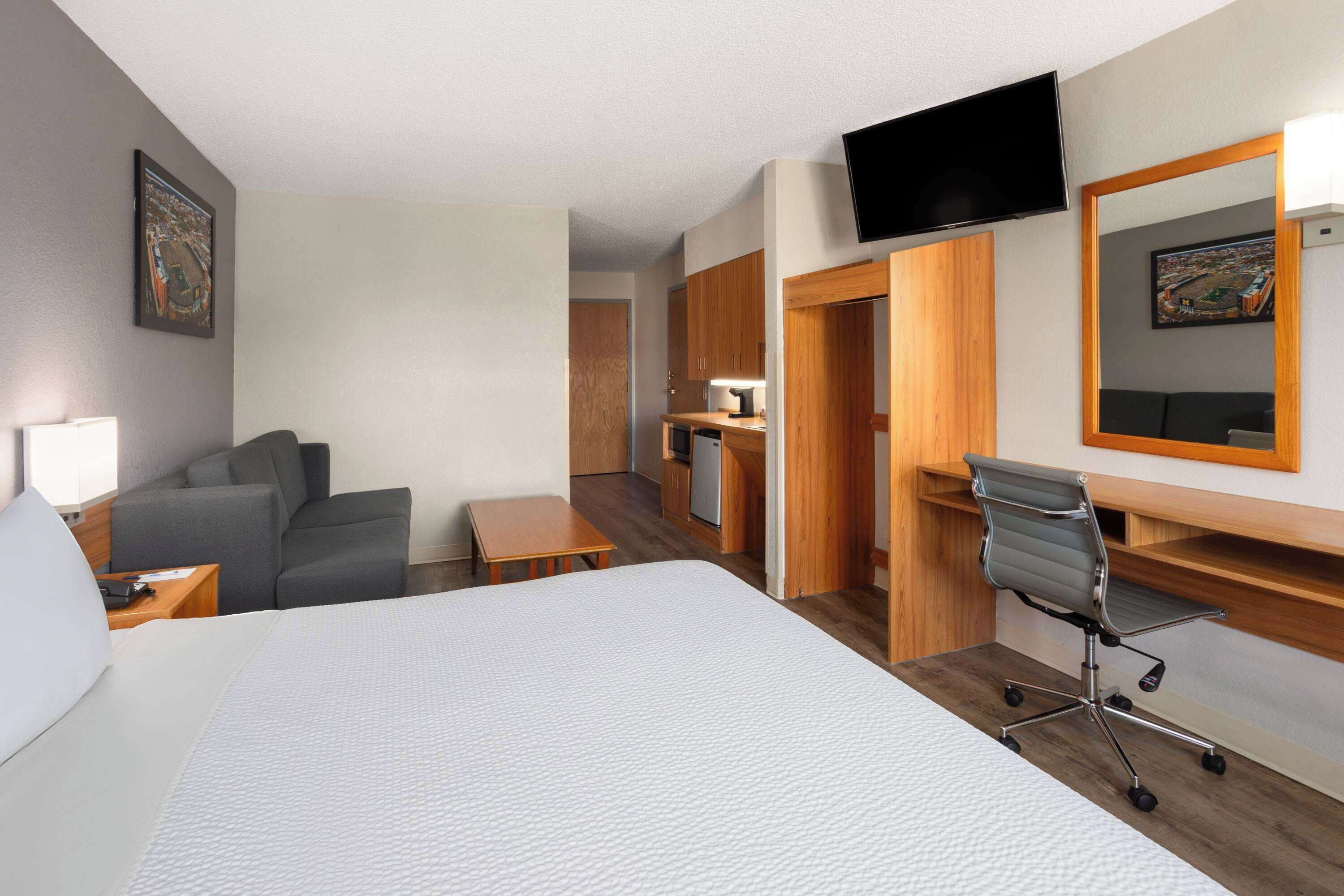 A hotel room with a large bed, a desk with a chair, a sofa, a television, and a mirror.