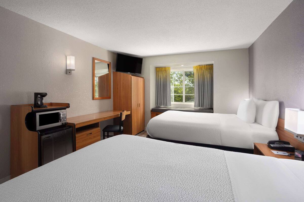 A hotel room with two beds, a desk with a microwave, a TV, and a window with curtains.
