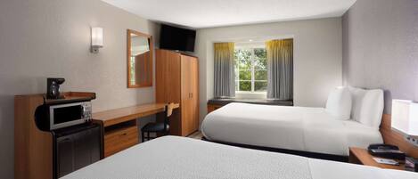 A hotel room with two beds, a desk with a microwave, a TV, and a window with curtains.