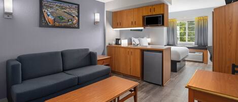 Ein kompaktes Hotelzimmer mit einer Schlafcouch, einem Holztisch, einer Küchenzeile und einem Bett.