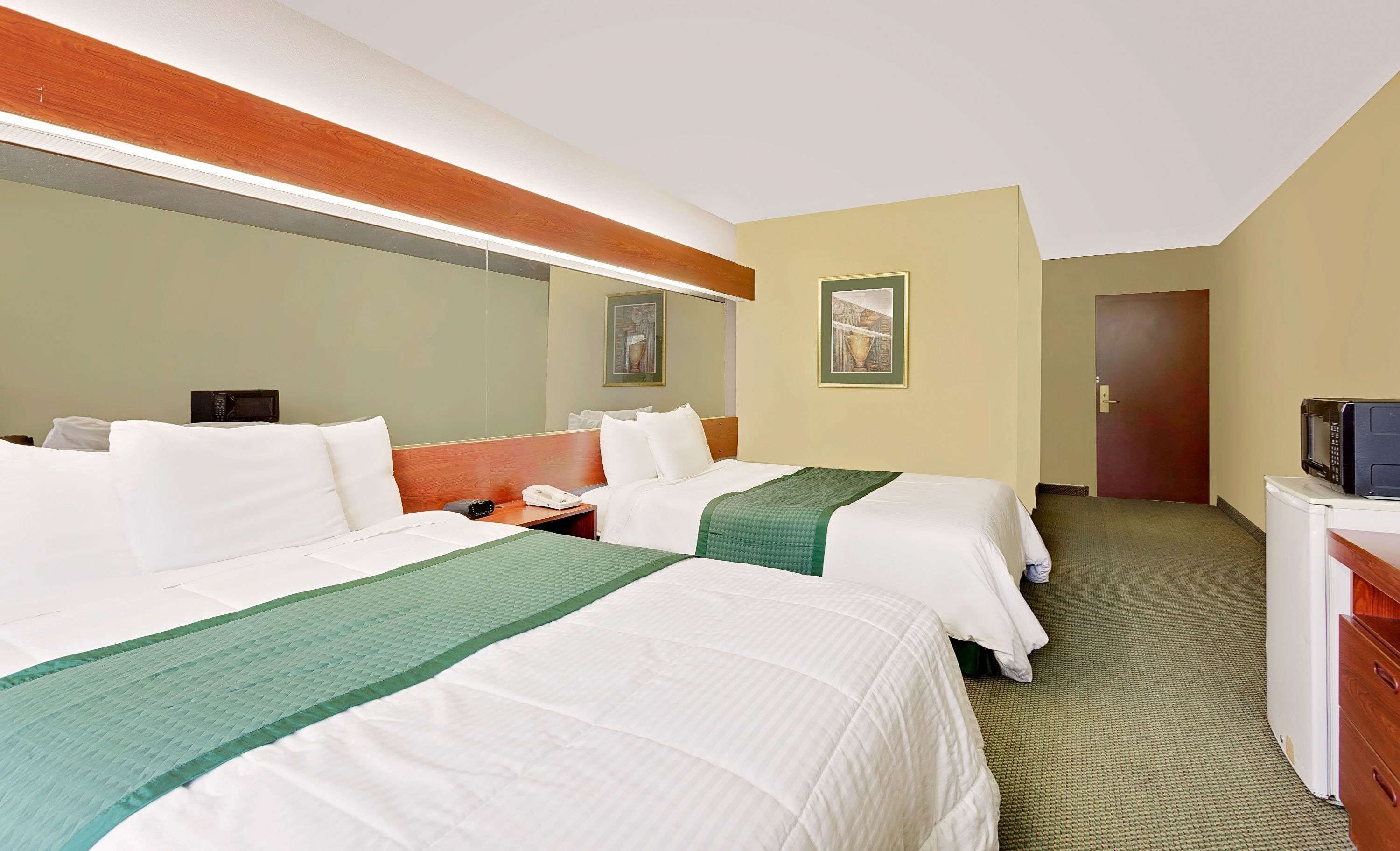 Una habitación de hotel con dos camas, un escritorio, un microondas y una puerta.
