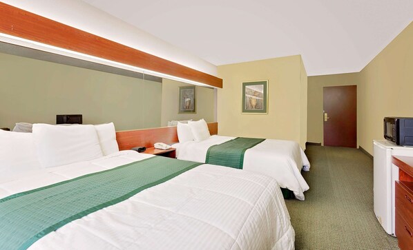 A hotel room with two beds, a desk, a microwave, and a door.