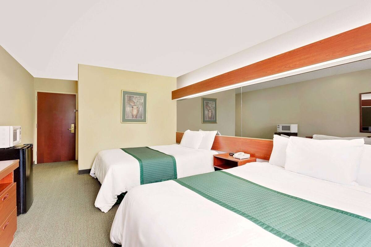 A hotel room with two beds, a desk, a microwave, and a door.