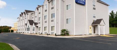 Un hôtel Microtel avec une rangée de chambres, un parking et un ciel dégagé.