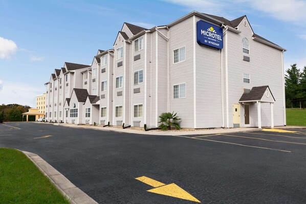 Un hotel Microtel con una fila de habitaciones, un estacionamiento y un cielo despejado.