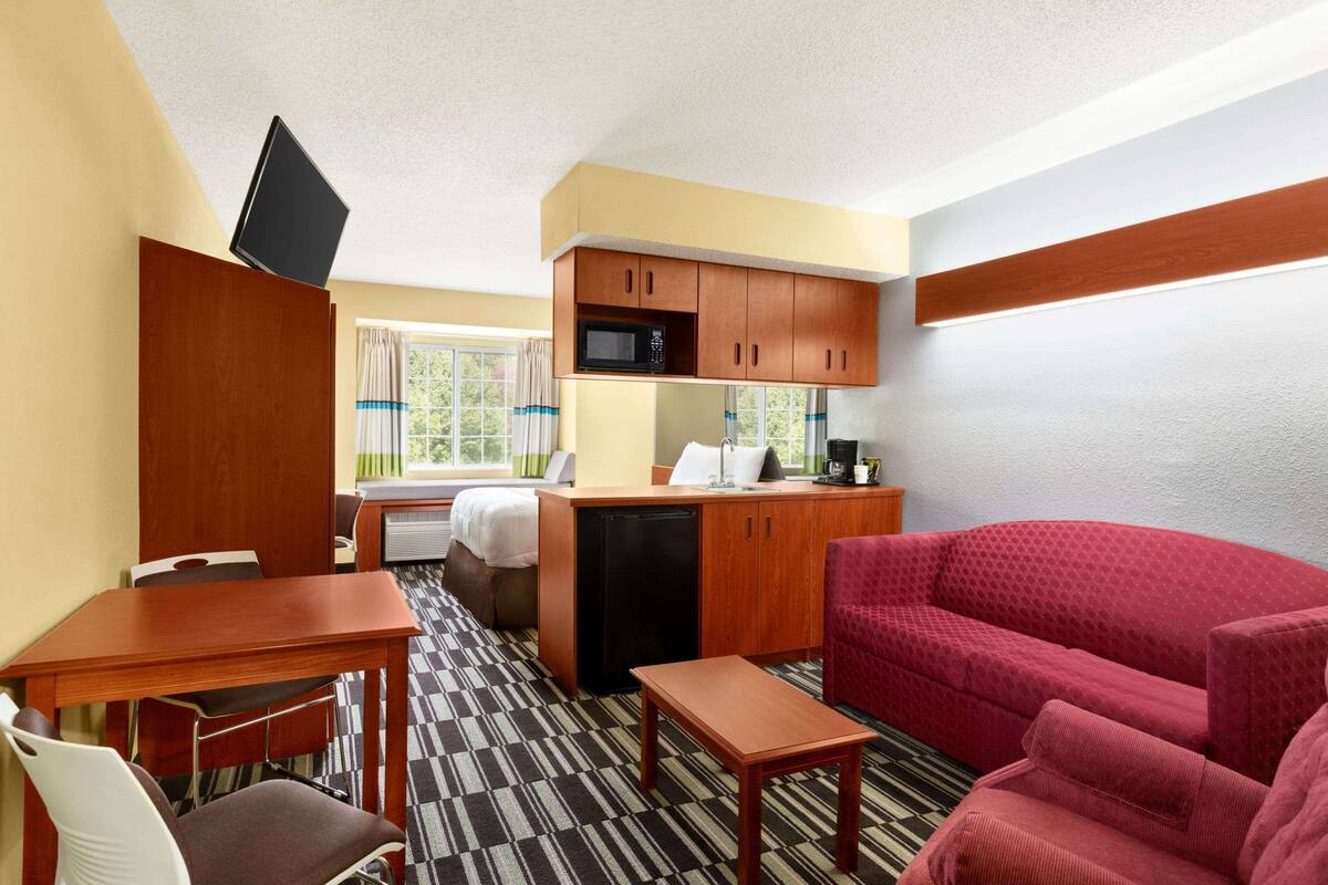 A compact hotel room with a kitchenette, a dining area, a sofa, and a bed.