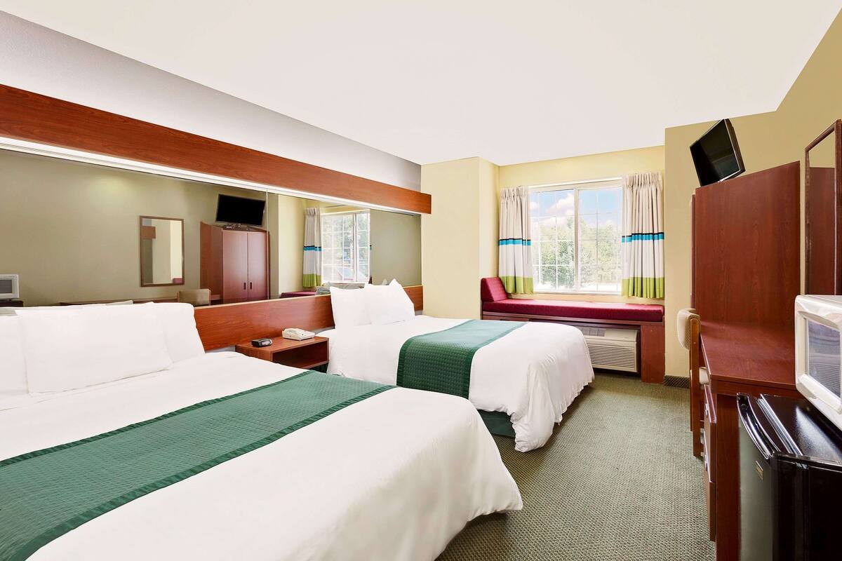 A hotel room with two beds, a desk, a TV, and a window with curtains.