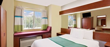 A hotel room with a large bed, a bench by the window, a desk, and a mirror.