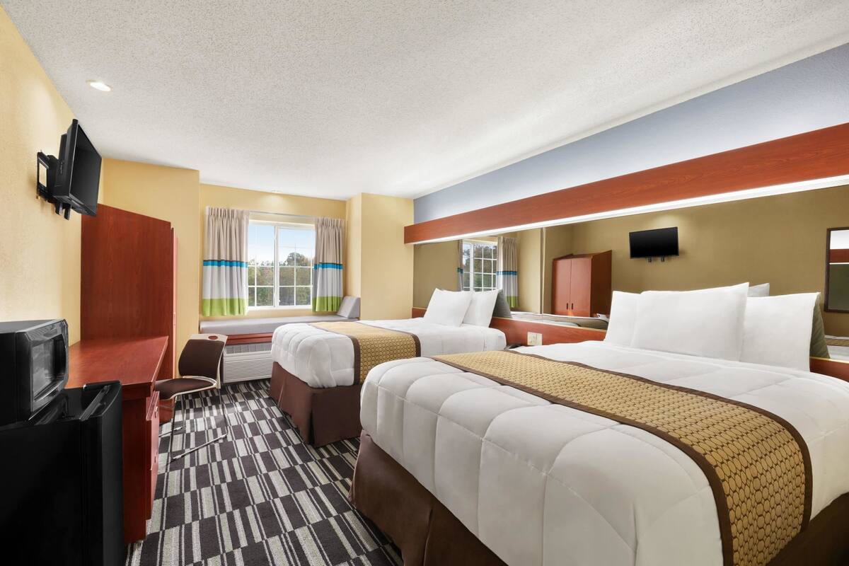 A hotel room with two beds, a desk, a TV, and a window with curtains.