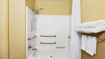 Un baño moderno con bañera, ducha y barras de apoyo. Hay toallas en un perchero y una cortina de ducha.