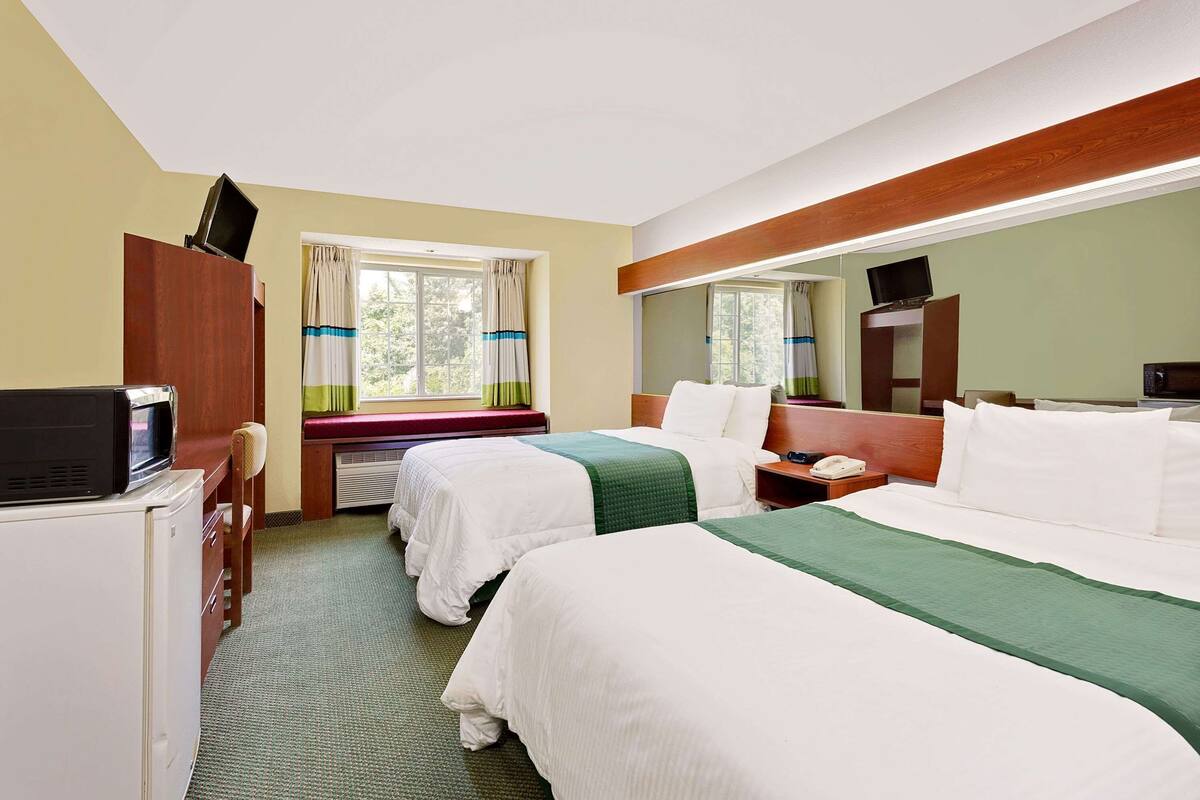 A hotel room with two beds, a desk with a TV, a microwave, and a window with curtains.