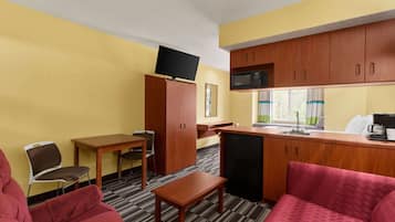 A compact hotel room with a kitchenette, a sofa, a small table, and a TV mounted on the wall.
