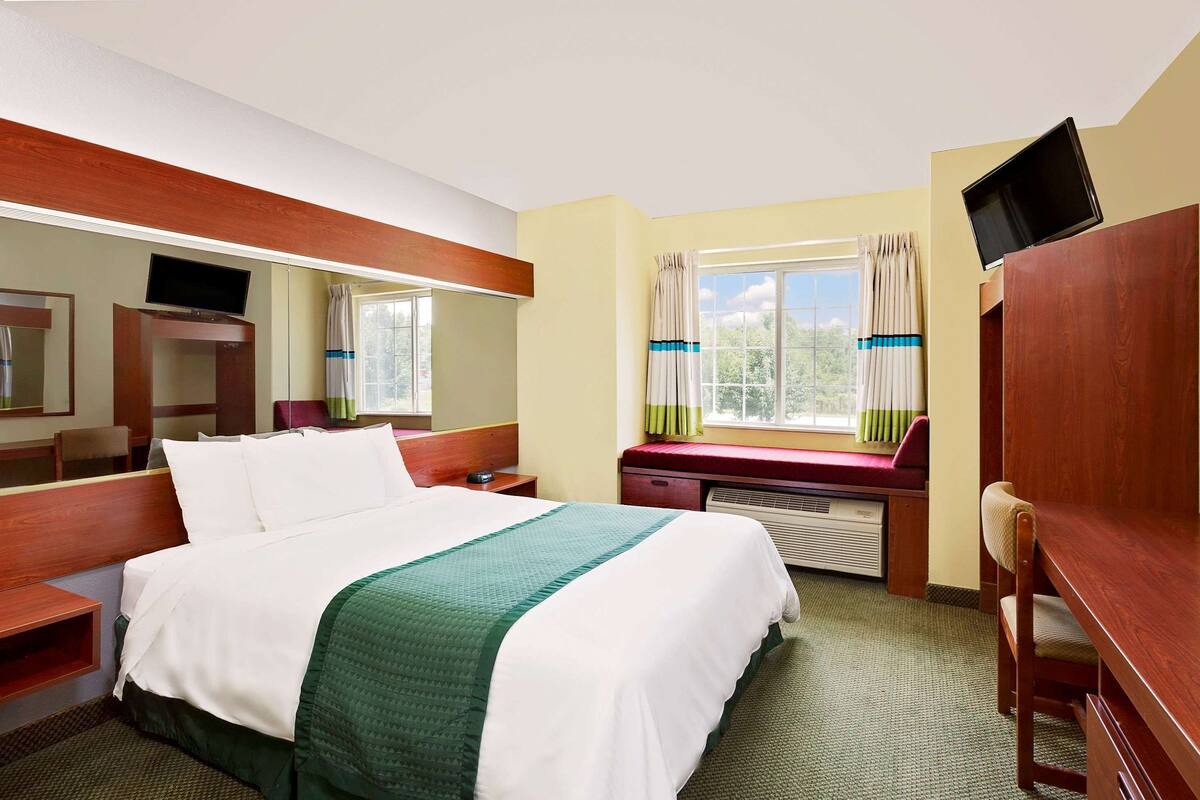 A hotel room with a bed, a desk, a chair, a TV, and a window with curtains.