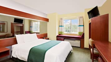 Una habitación de hotel con cama, escritorio, silla, televisor y ventana con cortinas.