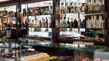A bar area with multiple shelves of liquor bottles, framed pictures on the wall, and a display case with various food items.