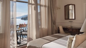 A spacious bedroom with a large bed, a chandelier, a view of the outdoors, and a desk with a lamp. - Amadria Park Hotel Milenij  (Opatija)