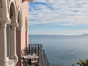 A balcony with a table and chairs overlooking a calm sea. - Amadria Park Hotel Milenij  (Opatija)