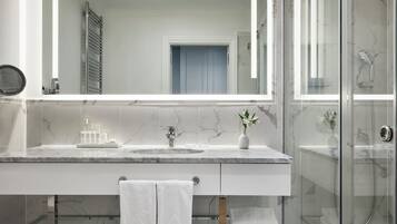 A modern bathroom with a large mirror, marble countertops, a glass shower enclosure, and a towel rack.