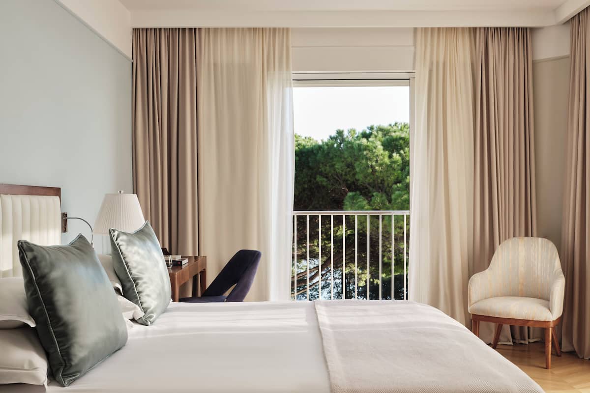 Una habitación de hotel con una cama grande, una silla, un escritorio y vistas a árboles por la ventana.